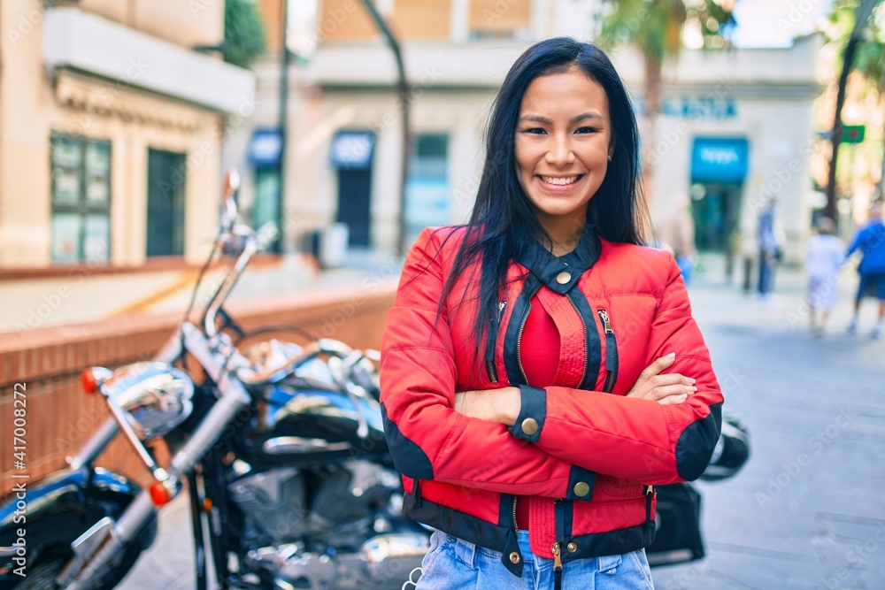 Young latin woman smiling happy standing over motorcycle at the city.