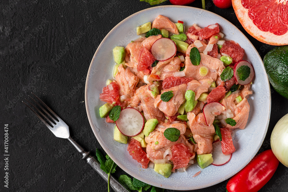 Chilean salmon seviche with grapefruit, avocado, radish, onion and mint in a plate with fork on black background. top view Chilean salmon seviche with grapefruit, avocado, radish, onion and mint in a plate with fork on black background. top view