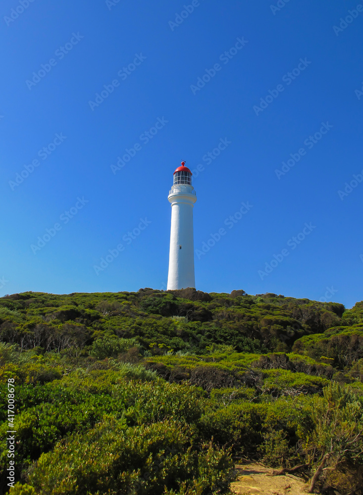 lighthouse on the coast surrounded by green bushes under a very blue sky