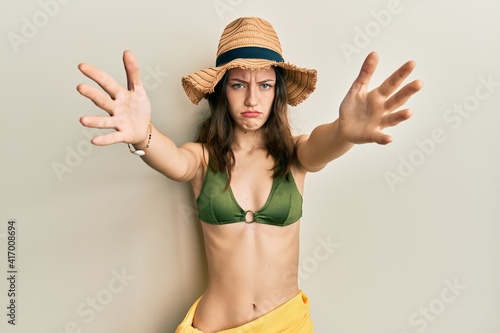 Young brunette woman wearing bikini and hat with open arms hugging depressed and worry for distress, crying angry and afraid. sad expression.