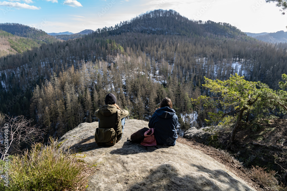 Fototapeta premium Two hikers enjoying the beautiful view near the edge of a cliff on a big rock. Taken in the Sächsische Schweiz rural district near Dresden, Germany