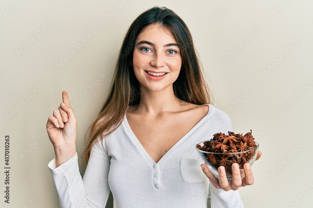 Young caucasian woman holding bowl of star anise smiling happy pointing with hand and finger to the side Young caucasian woman holding bowl of star anise smiling happy pointing with hand and finger to the side