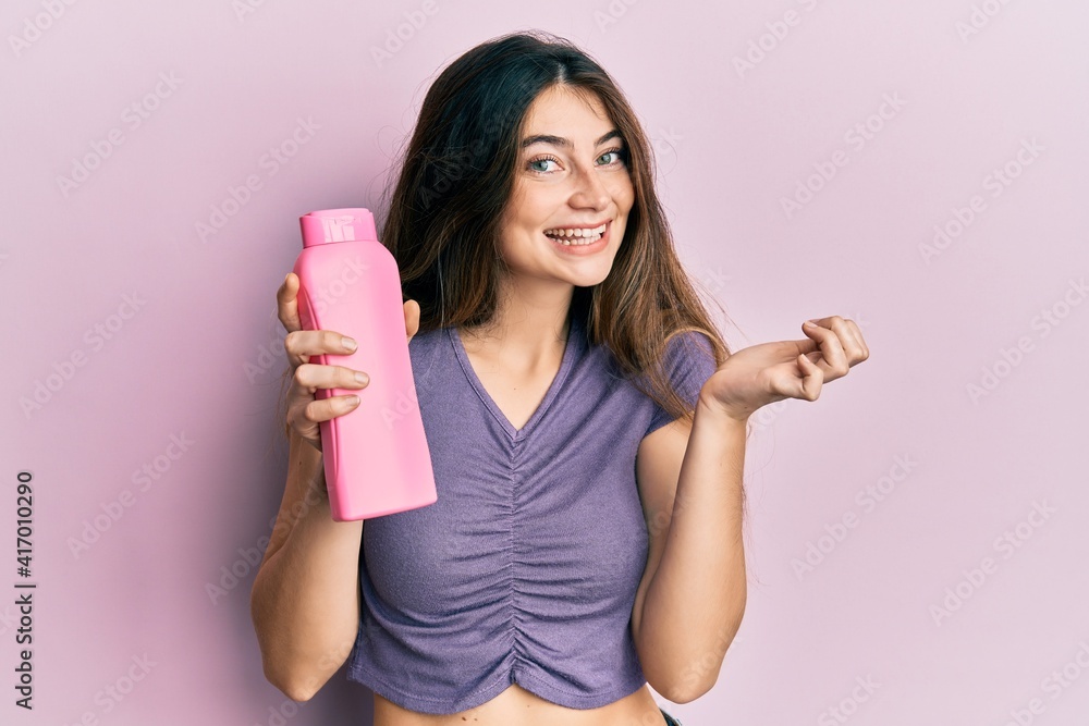 Young caucasian woman holding shampoo bottle screaming proud, celebrating victory and success very excited with raised arm Young caucasian woman holding shampoo bottle screaming proud, celebrating victory and success very excited with raised arm