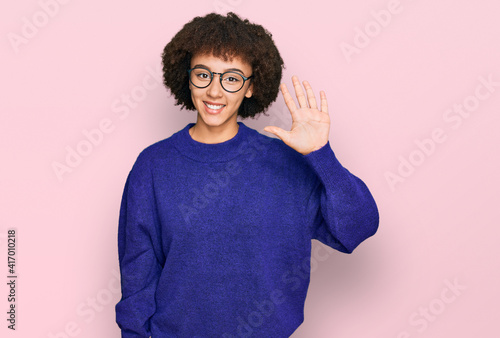 Young hispanic girl wearing casual winter sweater and glasses showing and pointing up with fingers number five while smiling confident and happy. © Krakenimages.com