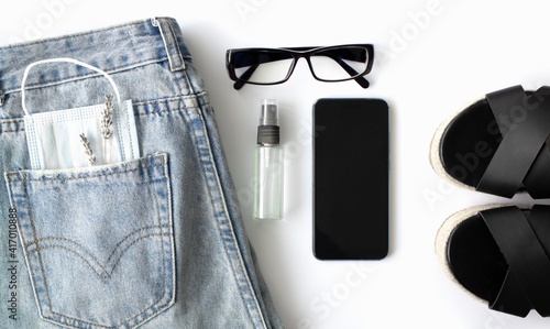 flat lay of women's things and accessories on a white background. Blue jeans, glasses, medical mask.