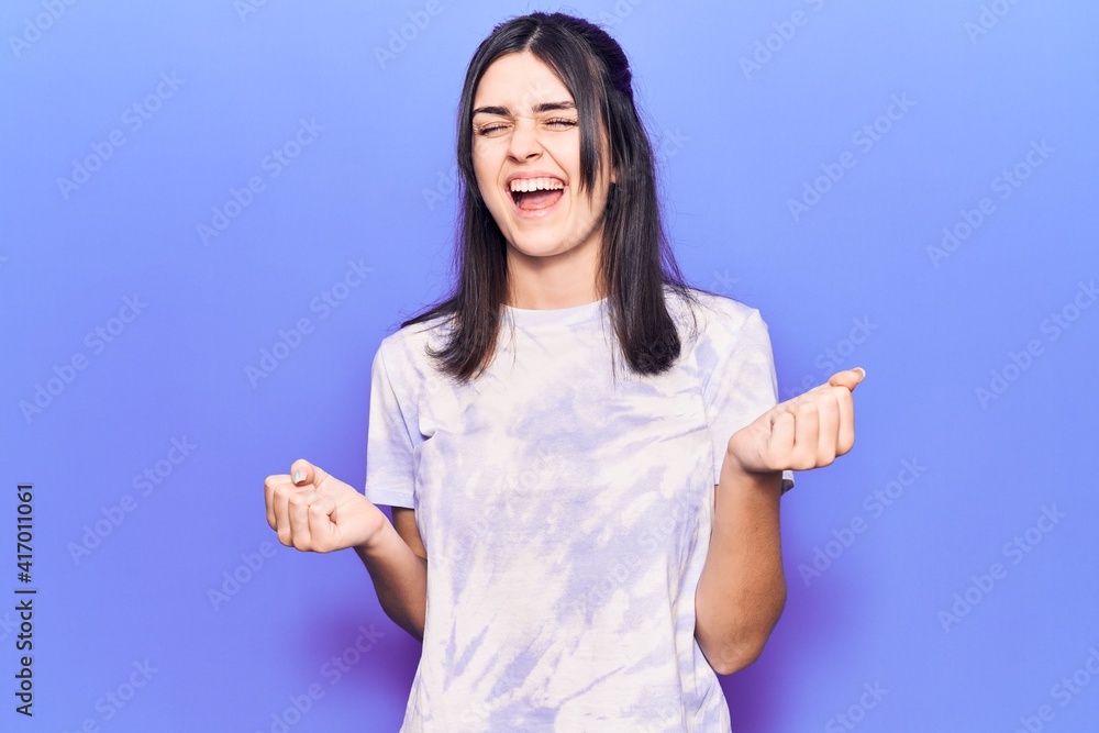 Young beautiful girl wearing casual t shirt celebrating surprised and amazed for success with arms raised and eyes closed Young beautiful girl wearing casual t shirt celebrating surprised and amazed for success with arms raised and eyes closed