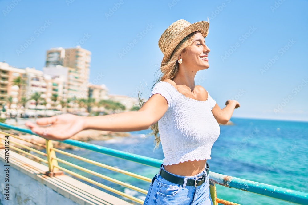 Young blonde tourist girl breathing with close eyes and open arms at the promenade.