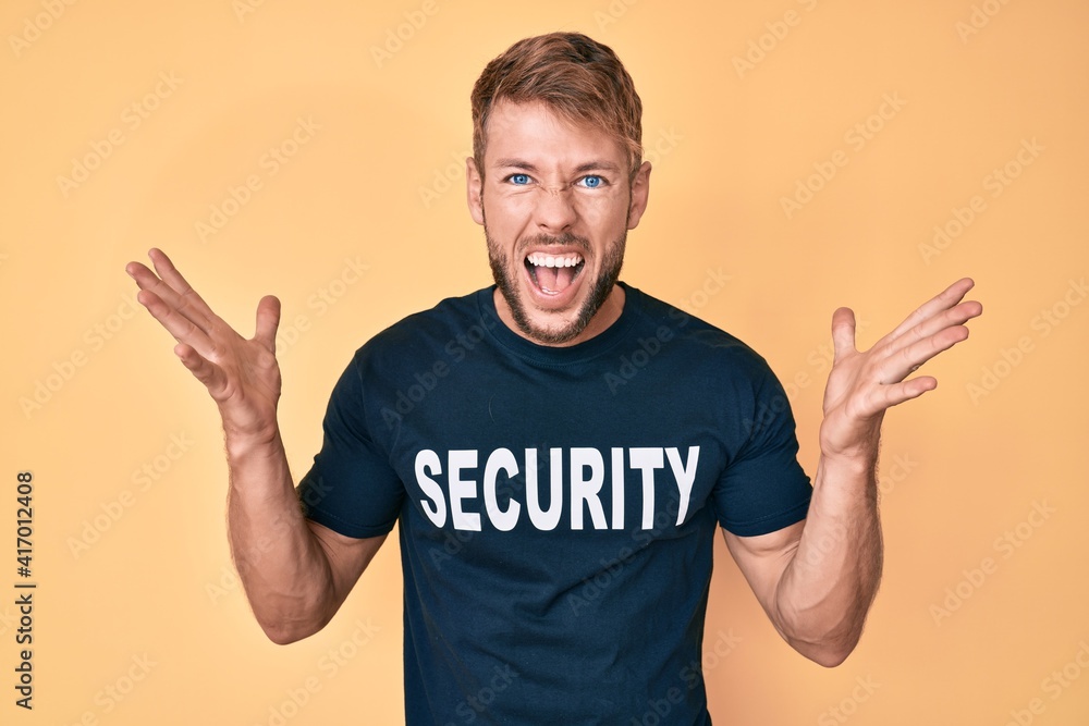 Young caucasian man wearing security t shirt celebrating crazy and amazed for success with arms raised and open eyes screaming excited. winner concept Young caucasian man wearing security t shirt celebrating crazy and amazed for success with arms raised and open eyes screaming excited. winner concept