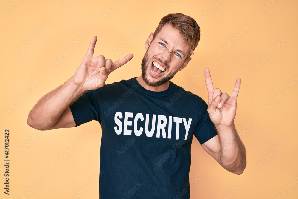 Fototapeta premium Young caucasian man wearing security t shirt shouting with crazy expression doing rock symbol with hands up. music star. heavy concept.