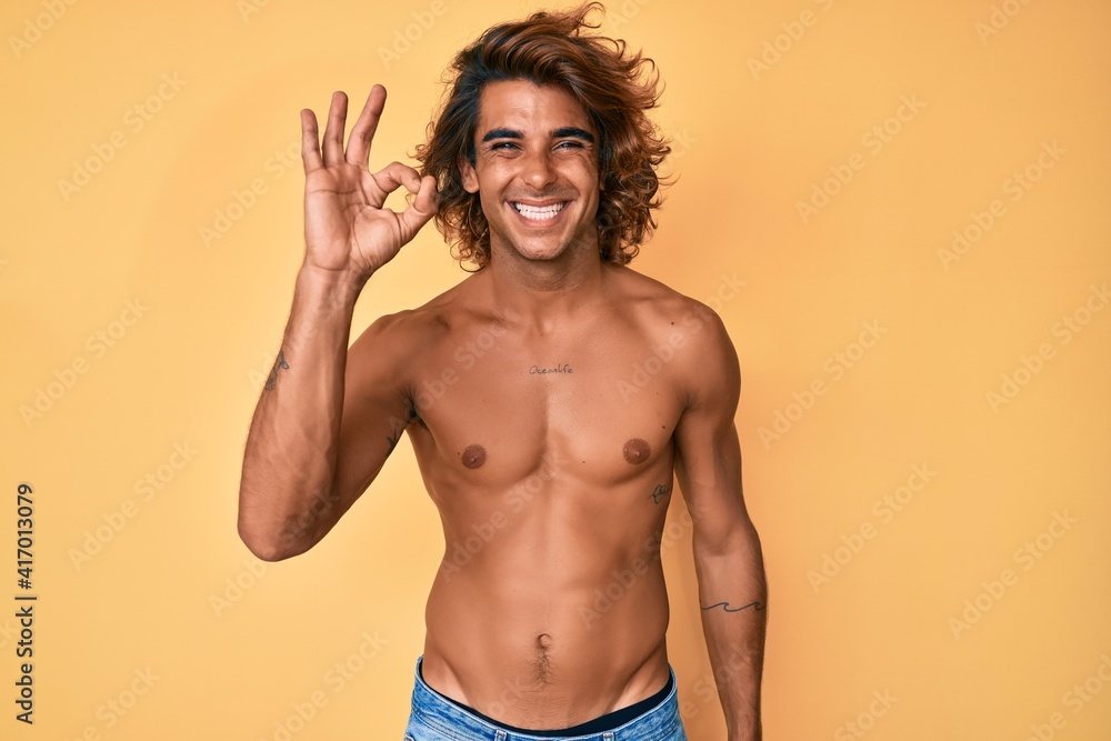 Fototapeta premium Young hispanic man standing shirtless smiling positive doing ok sign with hand and fingers. successful expression.