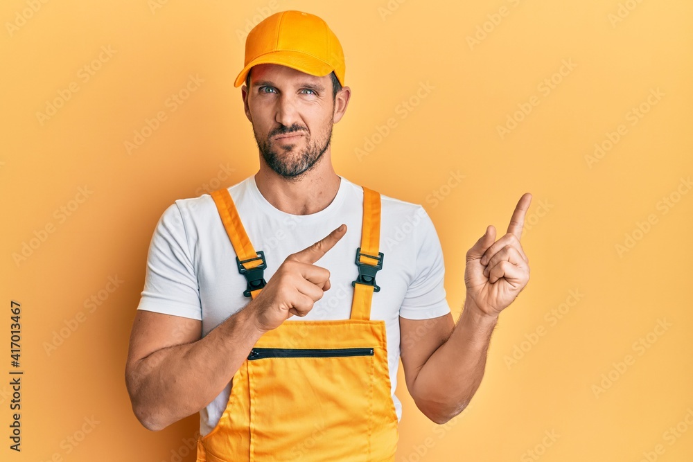 Young handsome man wearing handyman uniform pointing to the side clueless and confused expression. doubt concept. Young handsome man wearing handyman uniform pointing to the side clueless and confused expression. doubt concept.