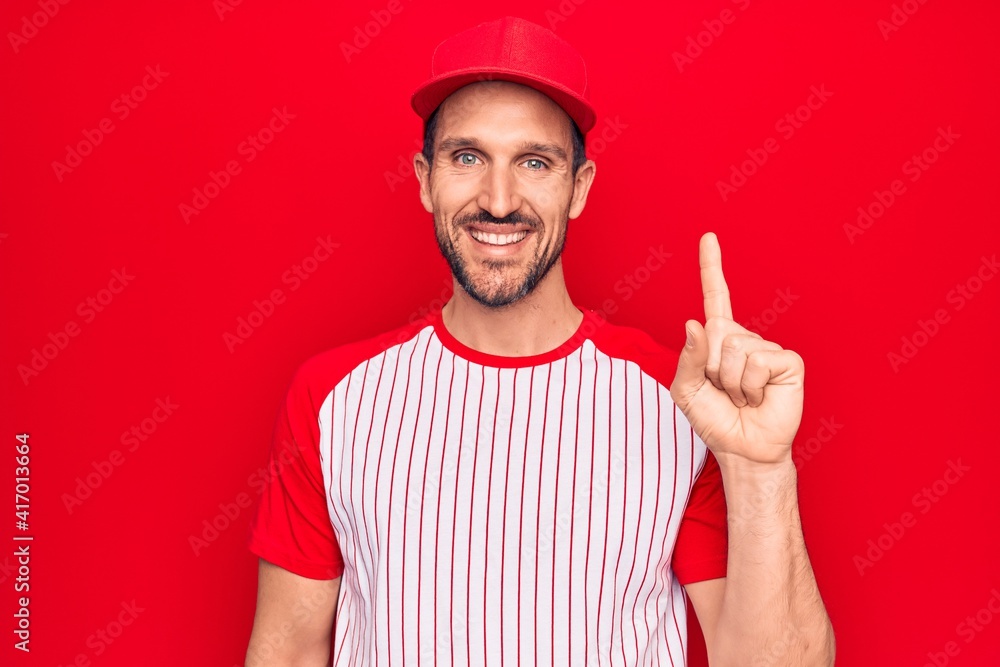 Young handsome player man wearing baseball sportswear over isolated red background smiling with an idea or question pointing finger up with happy face, number one Young handsome player man wearing baseball sportswear over isolated red background smiling with an idea or question pointing finger up with happy face, number one