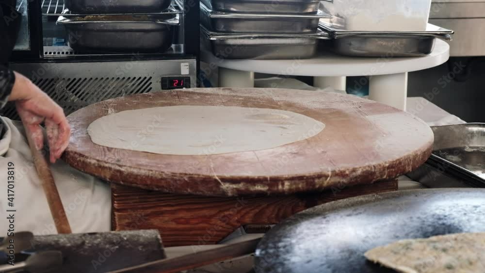 Turkish cook filling dough with cheese while cooking gozleme bread in restaurant kitchen in a hotel in Turkey. Process of making traditional pastry treat with filling for serving tourists as a snack. Turkish cook filling dough with cheese while cooking gozleme bread in restaurant kitchen in a hotel in Turkey. Process of making traditional pastry treat with filling for serving tourists as a snack.
