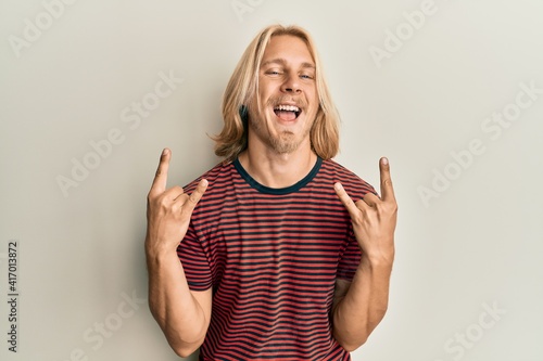 Caucasian young man with long hair doing rock gesture smiling and laughing hard out loud because funny crazy joke.