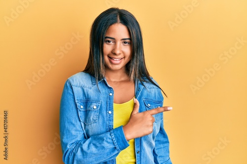 Young latin girl wearing casual clothes smiling cheerful pointing with hand and finger up to the side