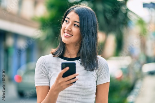 Young hispanic woman smiling happy using smartphone at the city.