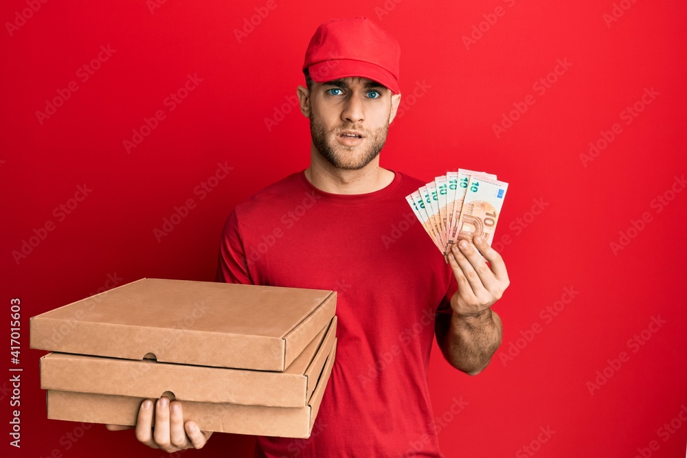 Young caucasian man holding take away food and 10 euros banknotes in shock face, looking skeptical and sarcastic, surprised with open mouth Young caucasian man holding take away food and 10 euros banknotes in shock face, looking skeptical and sarcastic, surprised with open mouth