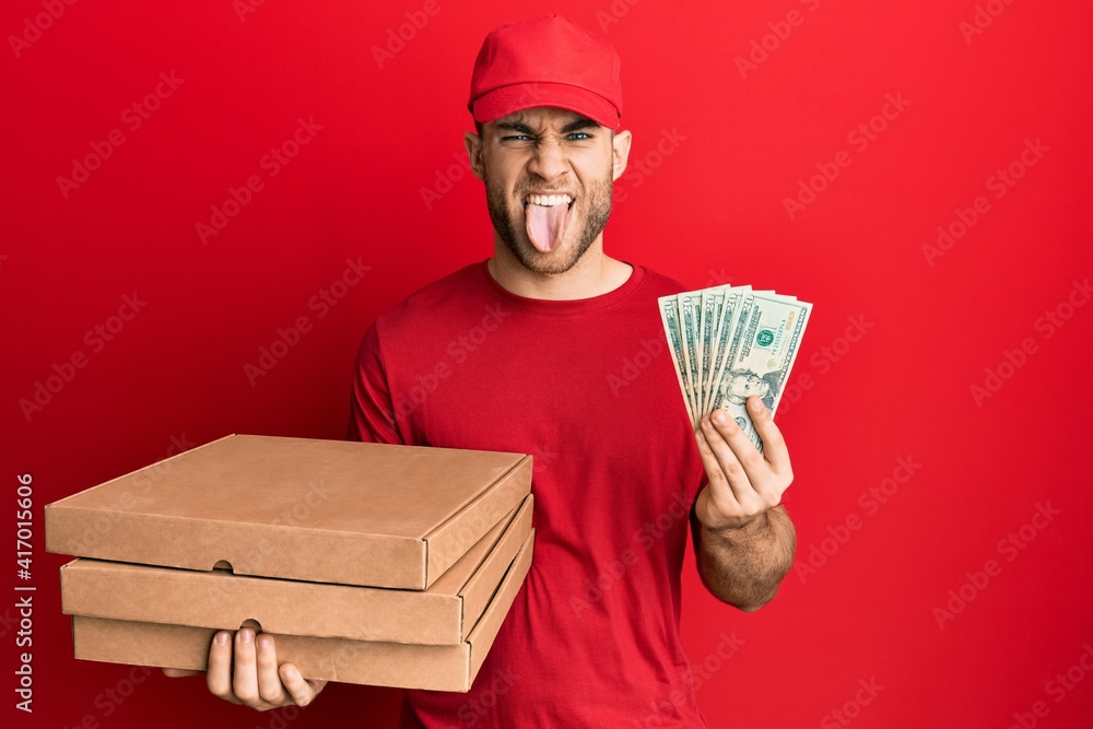 Young caucasian man holding take away food and 20 dollars sticking tongue out happy with funny expression. Young caucasian man holding take away food and 20 dollars sticking tongue out happy with funny expression.
