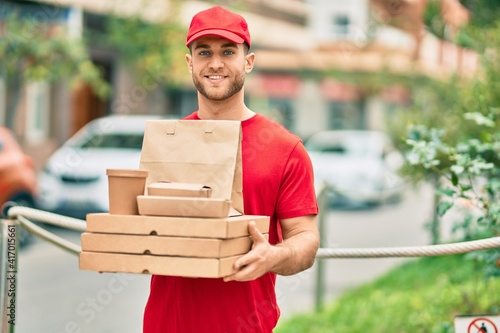 Принти на полотні Young caucasian deliveryman smiling happy holding delivery food at the city