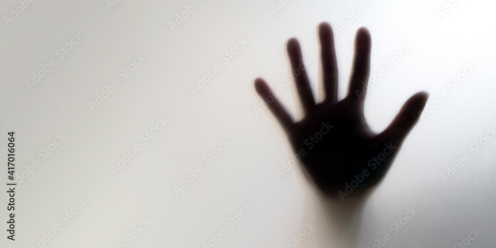 Silhouette of a blurred hand behind the glass. Concept of asking for help and domestic violence. Space to text
