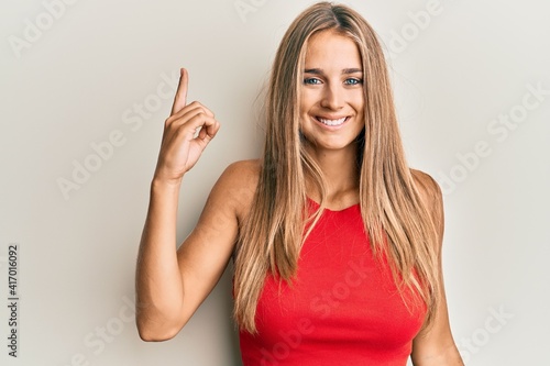 Young blonde woman wearing casual clothes pointing finger up with successful idea. exited and happy. number one.