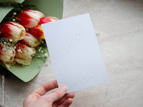 Greeting, post card, birthday mock up with hand holding card, marble background with the bouquet of tulips