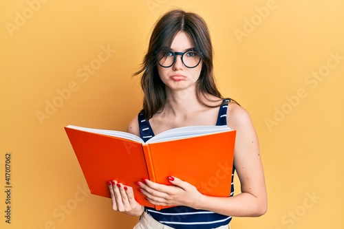 Young beautiful caucasian girl reading a book wearing glasses depressed and worry for distress, crying angry and afraid. sad expression.