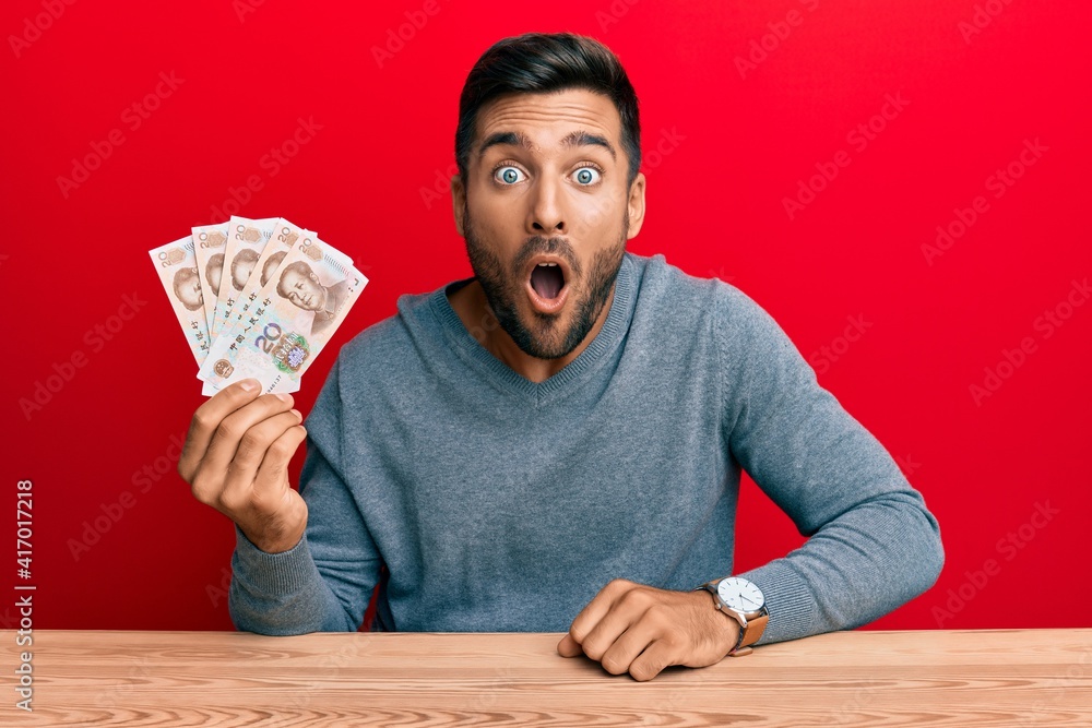 Handsome hispanic man holding yuan chinese banknotes scared and amazed with open mouth for surprise, disbelief face Handsome hispanic man holding yuan chinese banknotes scared and amazed with open mouth for surprise, disbelief face