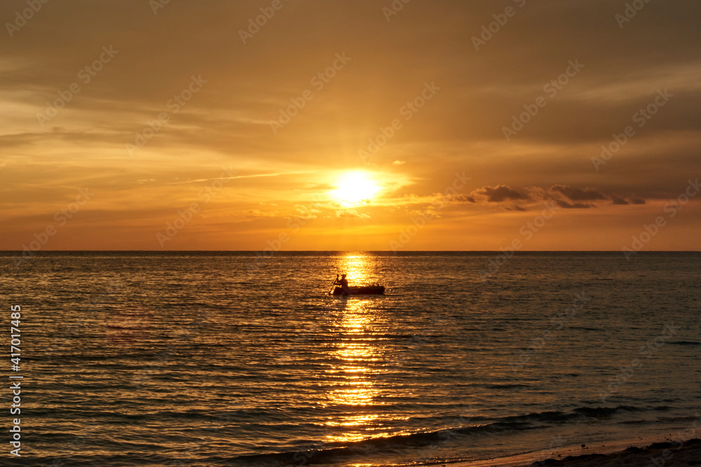 Cuba. Trinidad. Sunset in Ancon. A fisherman on a boat crosses the Sunny path