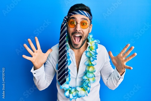 Young hispanic businessman wearing party funny style with tie on head celebrating crazy and amazed for success with arms raised and open eyes screaming excited. winner concept