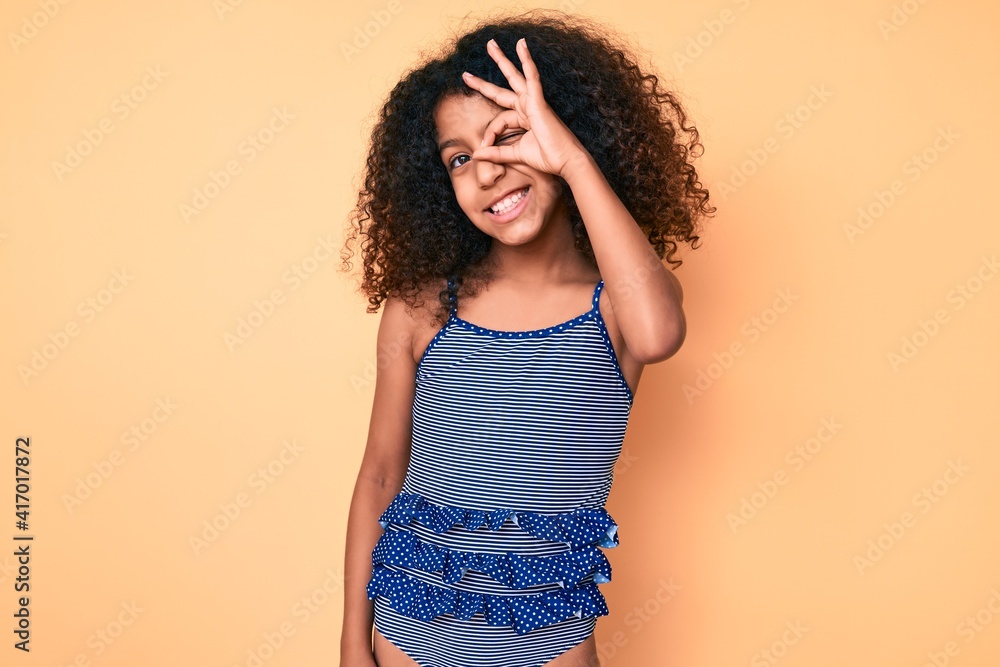 African american child with curly hair wearing swimwear smiling happy doing ok sign with hand on eye looking through fingers African american child with curly hair wearing swimwear smiling happy doing ok sign with hand on eye looking through fingers