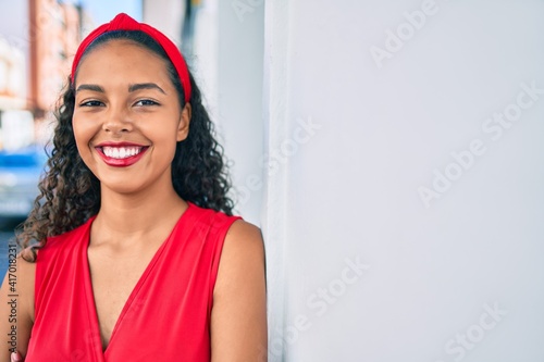 Young african american girl smiling happy leaning on the wall at city.