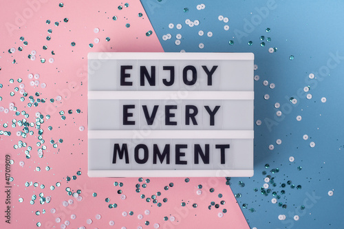 Fototapet Enjoy every moment - text on display lightbox on blue and pink background