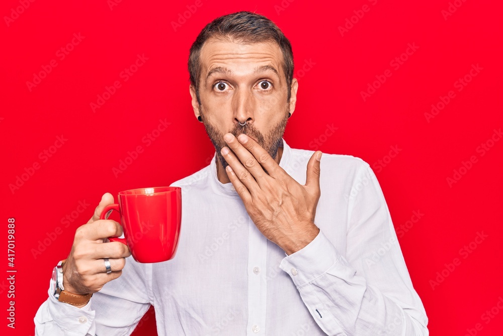Young handsome man holding coffee covering mouth with hand, shocked and afraid for mistake. surprised expression Young handsome man holding coffee covering mouth with hand, shocked and afraid for mistake. surprised expression