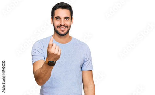 Young hispanic man wearing casual clothes beckoning come here gesture with hand inviting welcoming happy and smiling