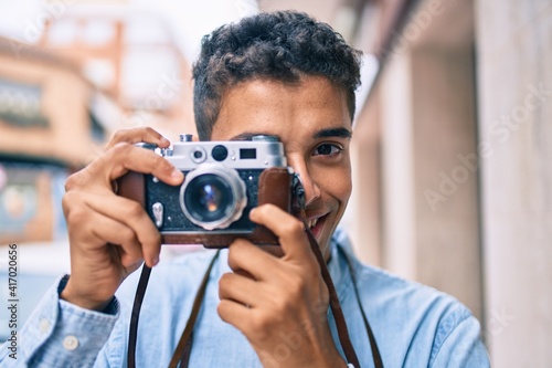 Young latin tourist man smiling happy using vintage camera walking at the city. © Krakenimages.com