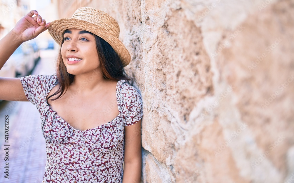 Young latin woman on vacation smiling happy leaning on the wall at street of city.