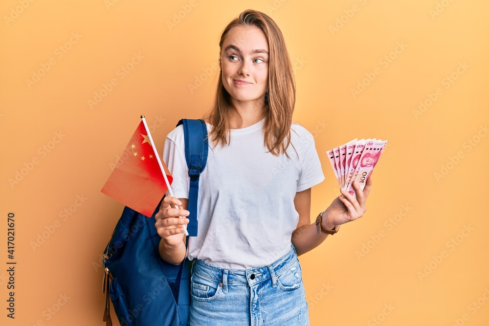 Beautiful blonde woman exchange student holding china flag and yuan banknotes smiling looking to the side and staring away thinking. Beautiful blonde woman exchange student holding china flag and yuan banknotes smiling looking to the side and staring away thinking.