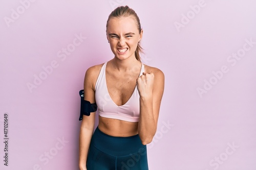Beautiful blonde woman wearing sportswear and arm band angry and mad raising fist frustrated and furious while shouting with anger. rage and aggressive concept. © Krakenimages.com