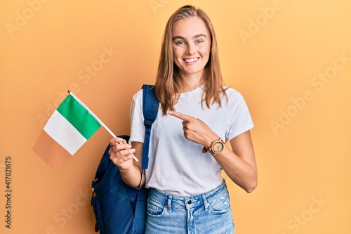 Beautiful blonde woman exchange student holding ireland flag smiling happy pointing with hand and finger