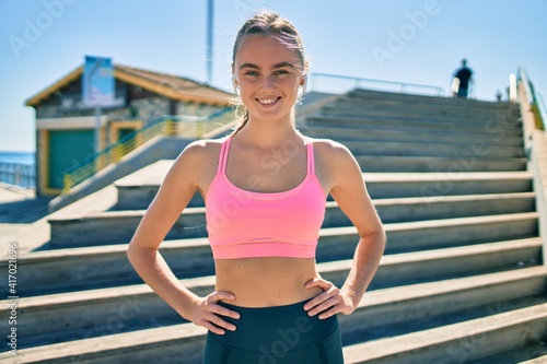 Young blonde sportswoman using earphones doing exercise at the city