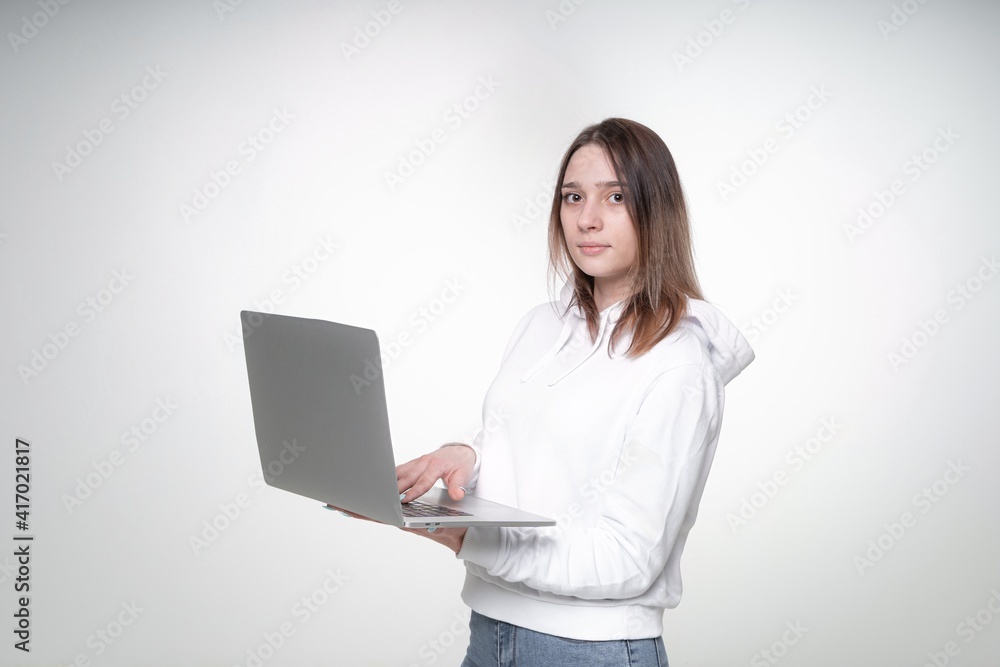 Young sweet student with fair hair is holding a laptop, typing on it, white studio background Young sweet student with fair hair is holding a laptop, typing on it, white studio background