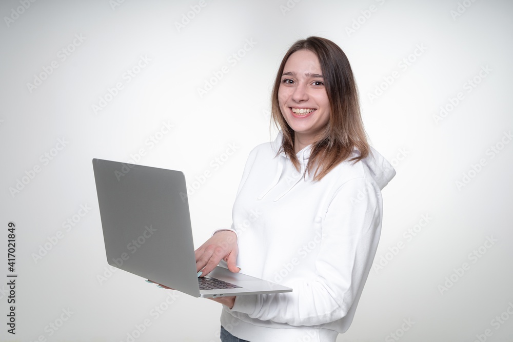Teenage girl is smiling widely, while typing in a laptop, waist-height photoshoot in a studio Teenage girl is smiling widely, while typing in a laptop, waist-height photoshoot in a studio