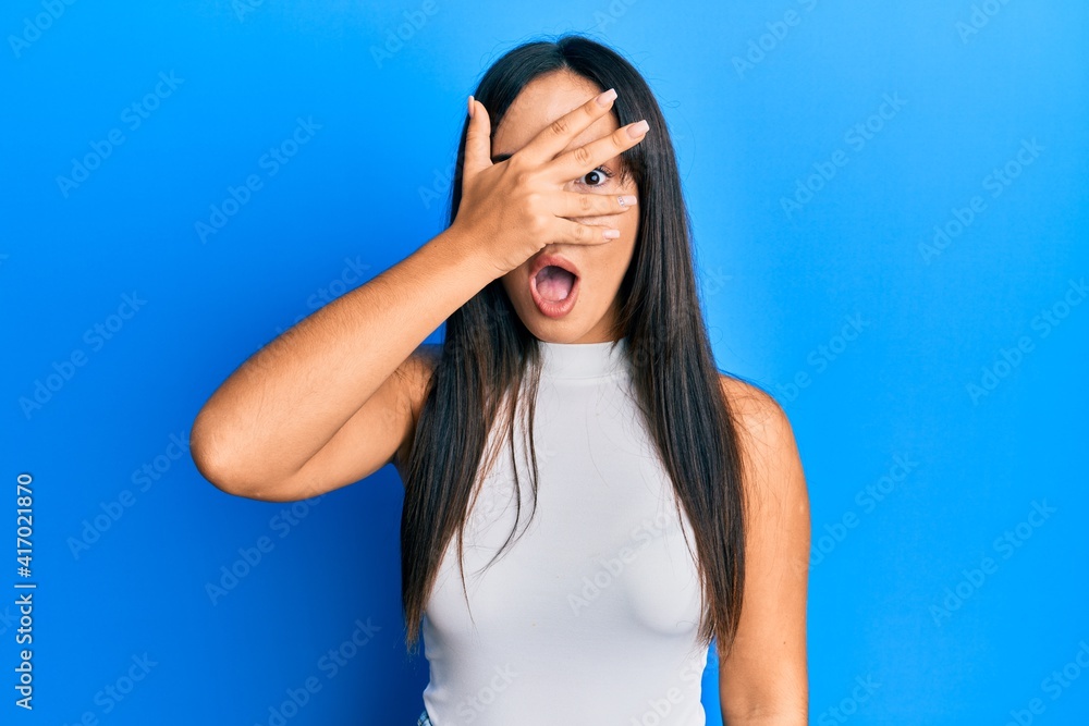 Young beautiful hispanic girl wearing casual clothes peeking in shock covering face and eyes with hand, looking through fingers afraid Young beautiful hispanic girl wearing casual clothes peeking in shock covering face and eyes with hand, looking through fingers afraid