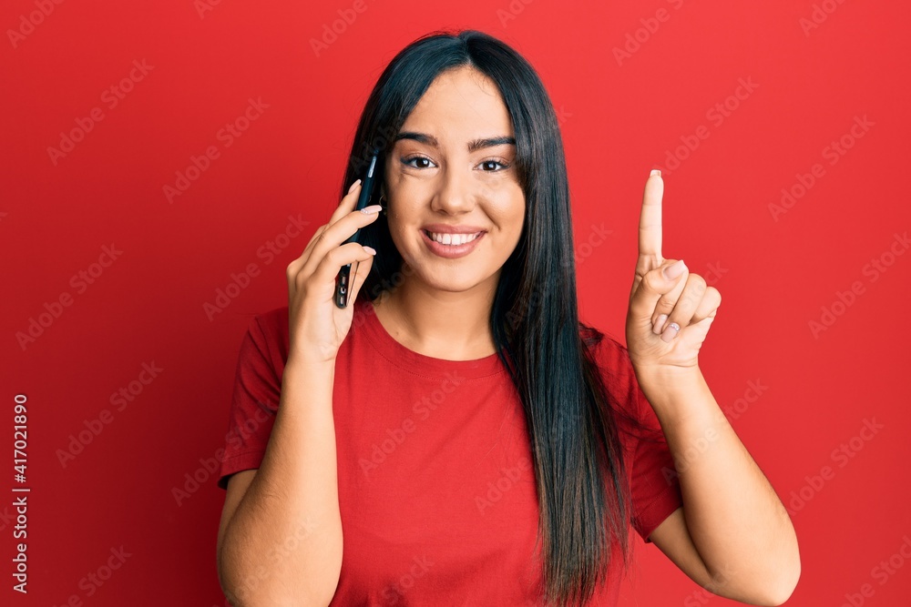 Young beautiful hispanic girl having conversation talking on the smartphone smiling with an idea or question pointing finger with happy face, number one Young beautiful hispanic girl having conversation talking on the smartphone smiling with an idea or question pointing finger with happy face, number one