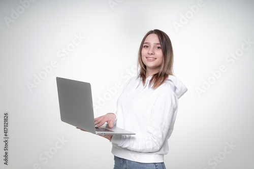 Teenage girl is smiling widely, while typing in a laptop, waist-height photoshoot in a studio © Tkachenko Alexey