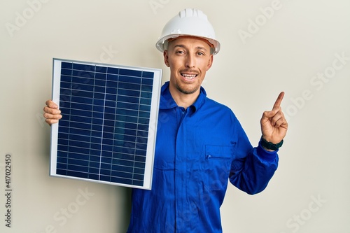 Bald engineer man with beard holding photovoltaic solar panel smiling happy pointing with hand and finger to the side