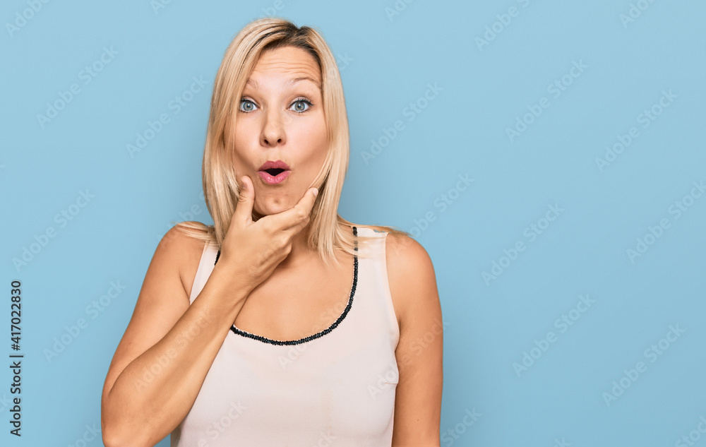 Middle age caucasian woman wearing casual clothes looking fascinated with disbelief, surprise and amazed expression with hands on chin Middle age caucasian woman wearing casual clothes looking fascinated with disbelief, surprise and amazed expression with hands on chin