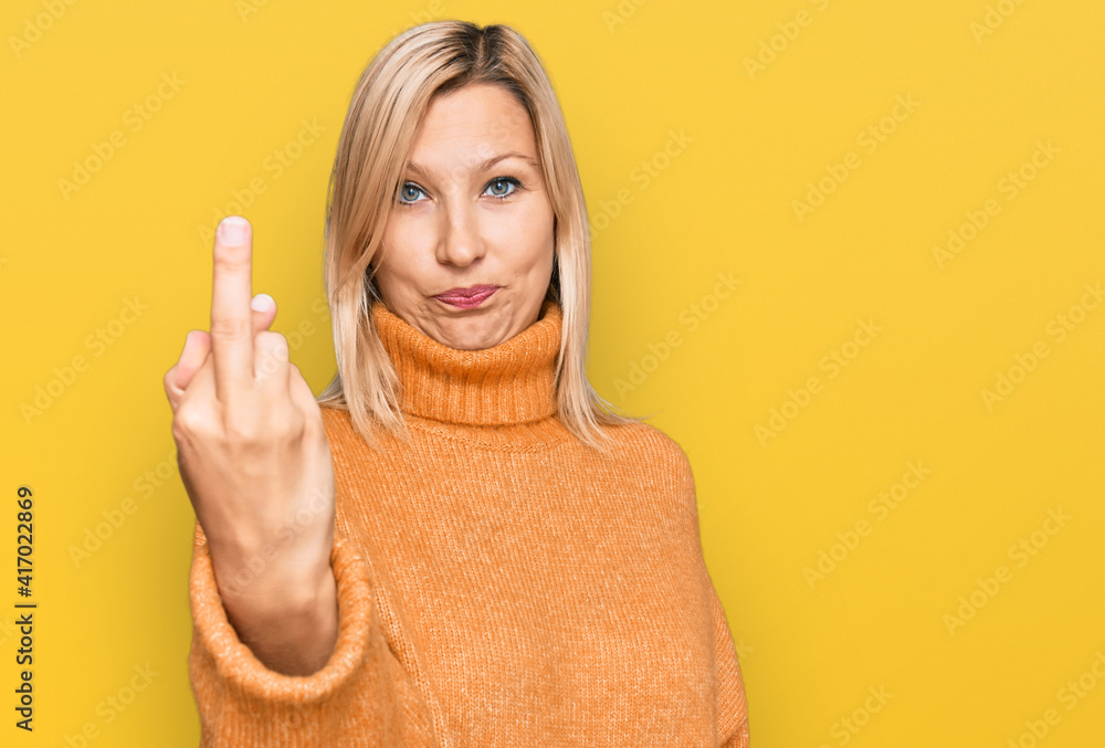 Middle age caucasian woman wearing casual winter sweater showing middle finger, impolite and rude fuck off expression Middle age caucasian woman wearing casual winter sweater showing middle finger, impolite and rude fuck off expression