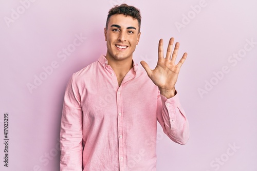 Hispanic young man wearing casual clothes showing and pointing up with fingers number five while smiling confident and happy.